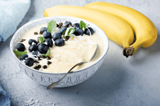 Nice cream banane, myrtilles & amandes dans un bol avec une cuillère et 2 bananes à côté du bol