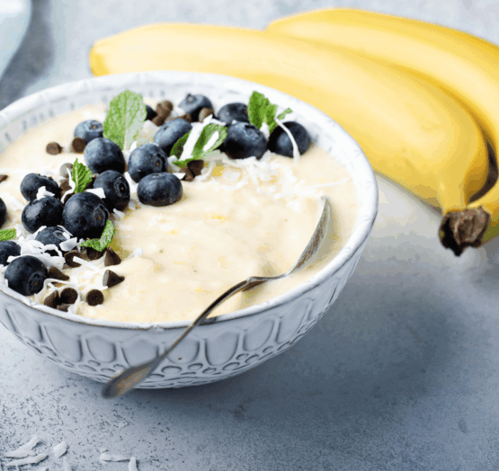 Nice cream banane, myrtilles & amandes dans un bol avec une cuillère et 2 bananes à côté du bol