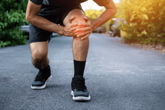 Homme en tenue de sport accroupi sur un chemin, tenant son genou douloureux à deux mains