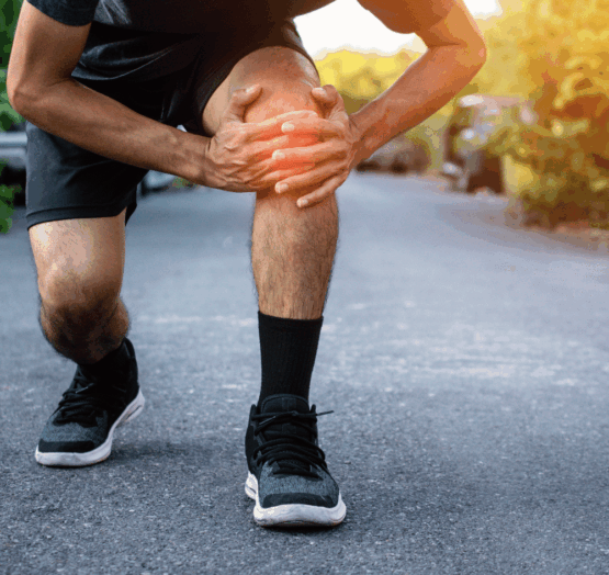 Homme en tenue de sport accroupi sur un chemin, tenant son genou douloureux à deux mains